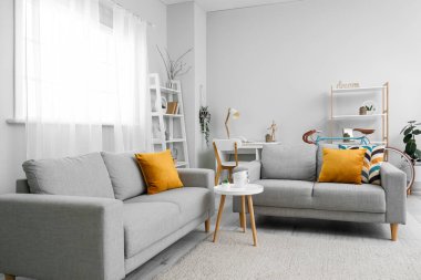 Interior of living room with grey sofas, coffee table, workplace and bicycle near window