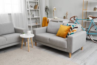 Interior of living room with grey sofas, coffee table, workplace and bicycle near window