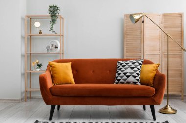 Interior of living room with brown sofa,  shelving unit, wooden folding screen and lamp near grey wall