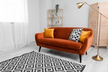 Interior of light living room with brown sofa, wooden folding screen and lamp near window