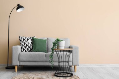 Interior of living room with grey sofa, table, lamp and houseplant near beige wall