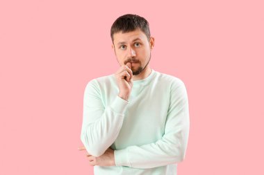 Pembe arka planda tırnaklarını yiyen yakışıklı bir adam.