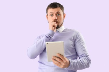 Handsome man with tablet computer biting nails on lilac background