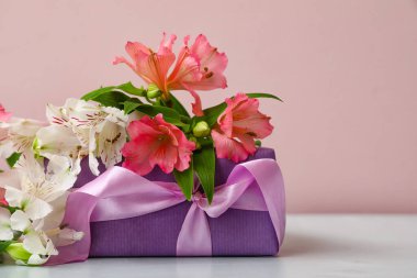 Beautiful alstroemeria flowers and gift box on table near color wall, closeup. Mother's day celebration