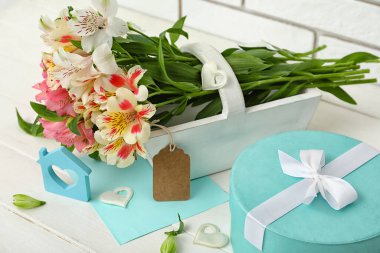 Beautiful alstroemeria flowers, gift box and decor on light wooden table, closeup. Mother's day celebration