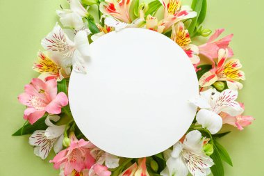 Composition with blank card and beautiful alstroemeria flowers on green background, closeup. Mother's day celebration