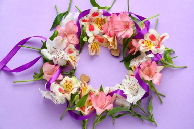 Wreath made of beautiful alstroemeria flowers and ribbon on lilac background. Mother's day celebration