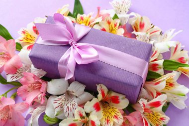 Beautiful composition with gift box and alstroemeria flowers on lilac background, closeup. Mother's day celebration