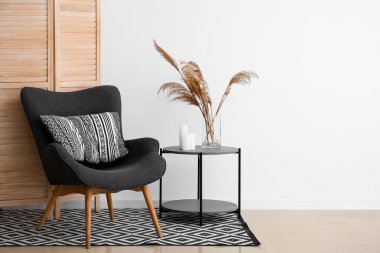 Interior of living room with folding screen, armchair and pampas grass in vase near white wall