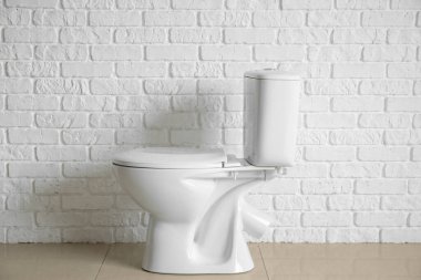 Modern toilet bowl near white brick wall