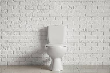 Modern toilet bowl near white brick wall