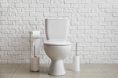 Modern toilet bowl near white brick wall