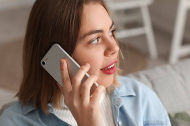 Evde akıllı telefonla konuşan genç bir kadın, yakın plan.