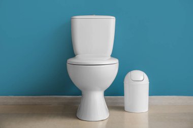 Ceramic toilet bowl and bin near blue wall