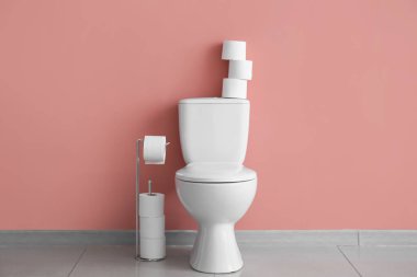 Ceramic toilet bowl and paper rolls near pink wall