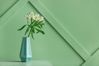 Vase with bouquet of alstroemeria flowers on green table near color wall