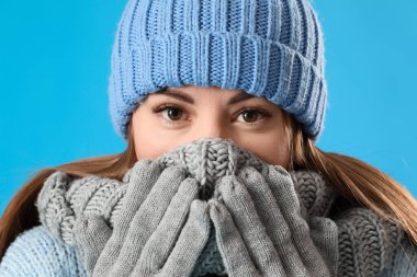 Donmuş genç kadın mavi arka planda kışlık giysiler içinde, yakın plan.