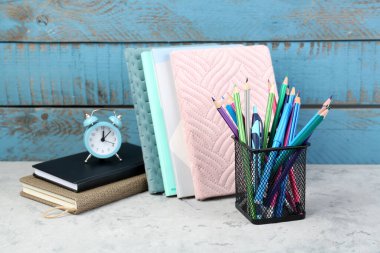 Stationery holder with notebooks and alarm clock on wooden background