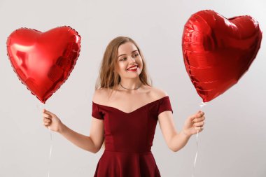 Happy young woman with heart-shaped balloons on light background. Valentine's Day celebration