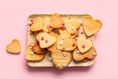 Plate with sweet heart shaped cookies and sprinkles on pink background. Valentines Day celebration