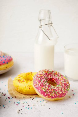 Parchment with delicious donuts and bottle of milk on white table