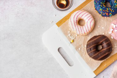Board with different delicious donuts on white table