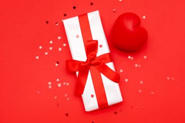 Composition with beautiful gift box, heart and sequins on red background. Valentines Day celebration