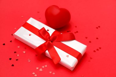 Composition with beautiful gift box, heart and sequins on red background. Valentines Day celebration