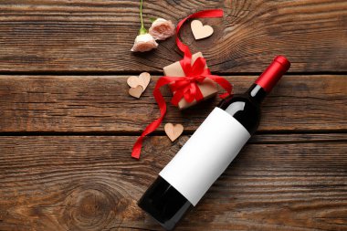 Composition with bottle of wine, gift and rose flowers on wooden background. Valentines Day celebration
