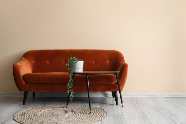 Интерьер гостиной с коричневым диваном, столом и комодом возле бежевой стены