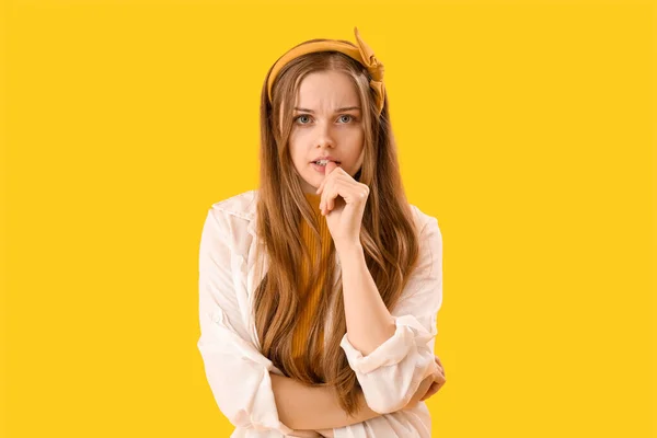 Young woman biting nails on yellow background