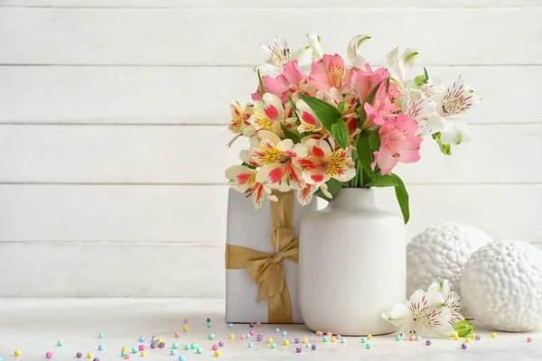 Vase with beautiful alstroemeria flowers, gift and decor on table near light wooden wall. Mother\'s day celebration