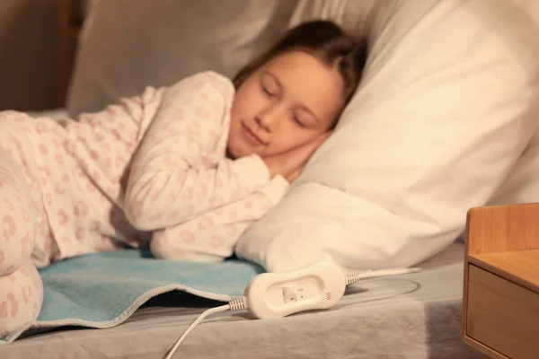 Little girl sleeping on electric heating pad in bedroom at night