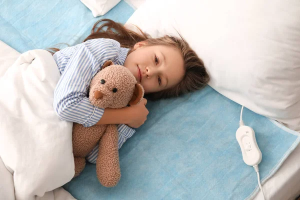 Little girl with toy lying on electric heating pad in bedroom