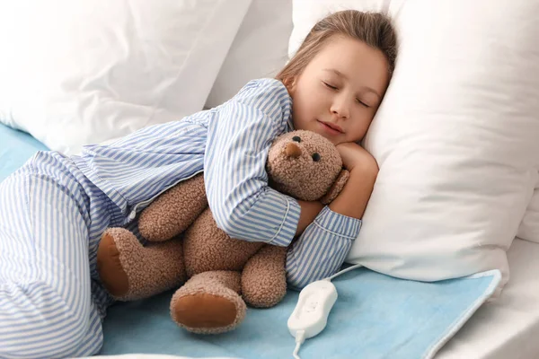 Little girl with toy sleeping on electric heating pad in bedroom