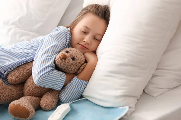 Little girl with toy sleeping on electric heating pad in bedroom