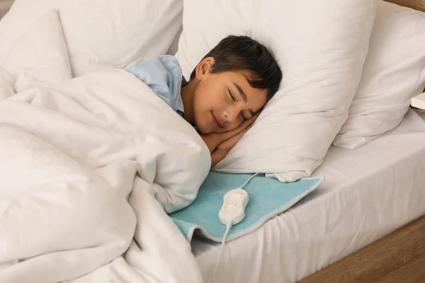 Little boy sleeping on electric heating pad in bedroom