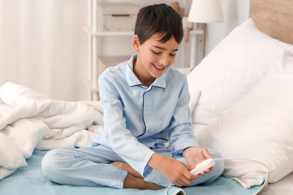 Little boy sitting on electric heating pad in bedroom