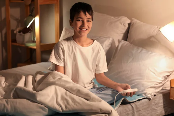 Little boy sitting on electric heating pad in bedroom at night