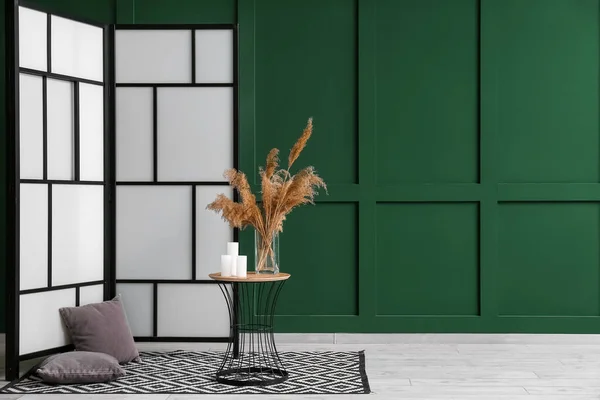 Folding screen, cushions and end table with pampas grass in vase near green wall