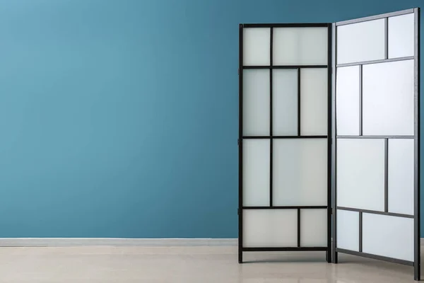 Stylish folding screen near blue wall
