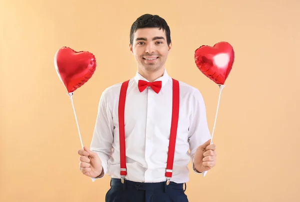 Young man with balloons on beige background. Valentine\'s Day celebration