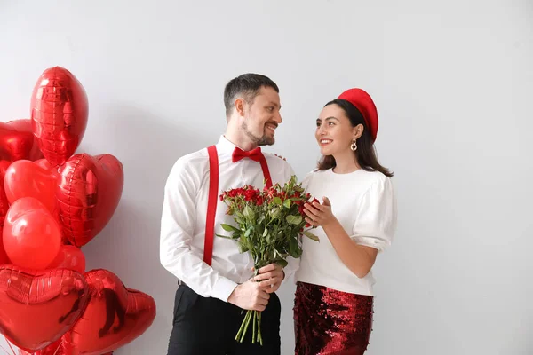 Happy couple in love with roses and balloons on grey background. Valentine's Day celebration