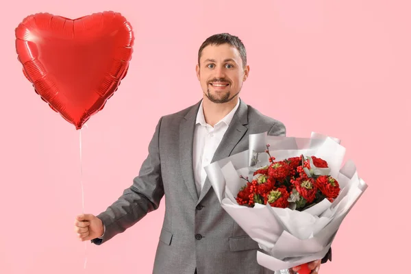 Handsome man with heart-shaped balloon and flowers on pink background. Valentine\'s Day celebration