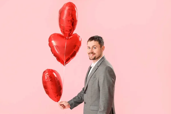 Handsome man with heart-shaped balloons on pink background. Valentine\'s Day celebration