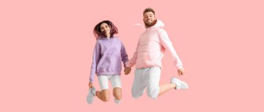 Cool jumping young couple in hoodies on pink background