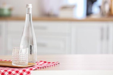 Board with bottle of water, glass and napkin on table in kitchen