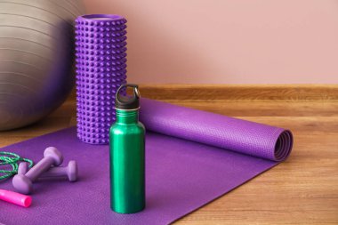 Sports water bottle with equipment on mat near pink wall