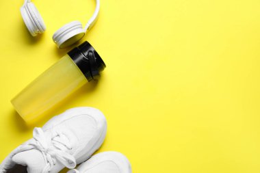 Sports water bottle with headphones and sneakers on yellow background