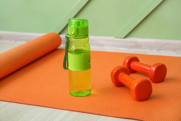 Sports water bottle with dumbbells on mat near green wall